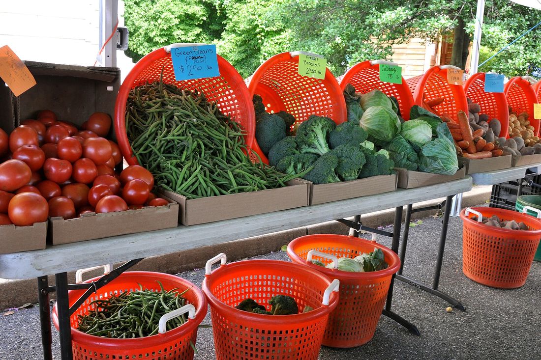 A farm stand table of tomatoes, beans, broccoli and cabbage with handwritten price signs