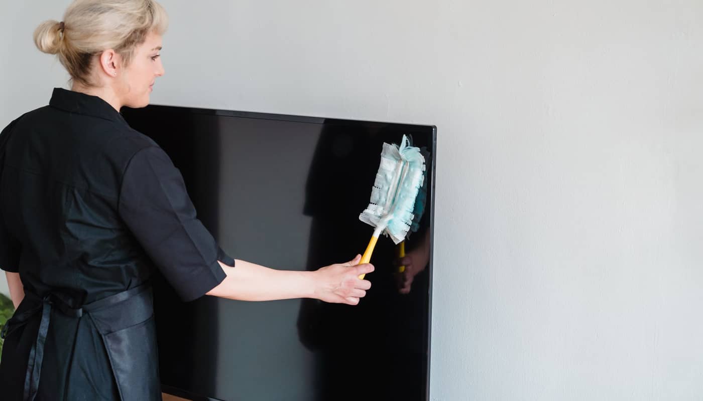 A cleaner dusting a television screen