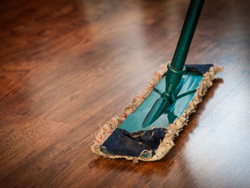 A dust mop being run across a dark hardwood floor